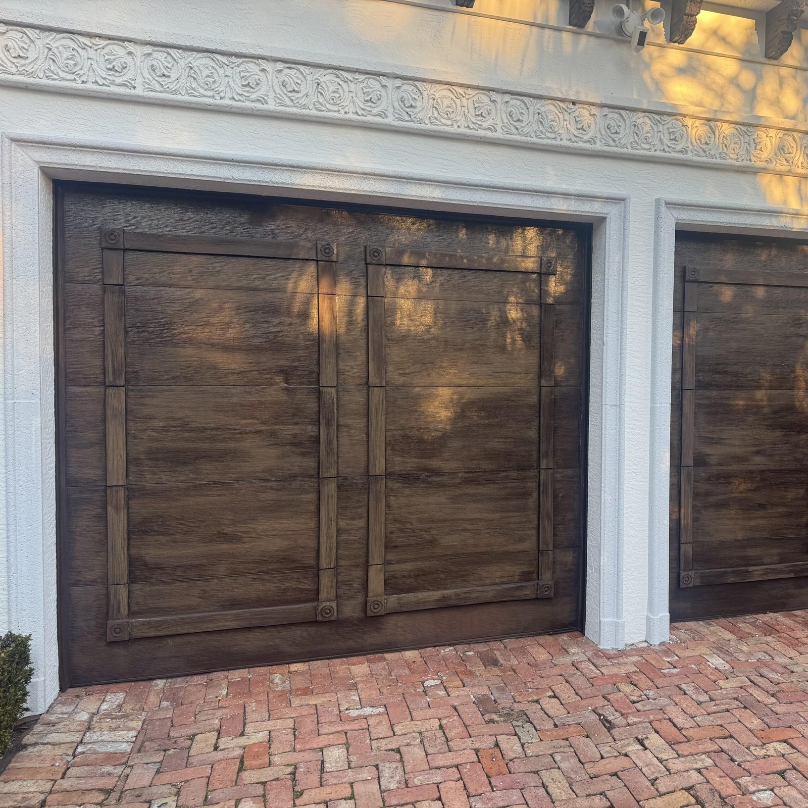 Finished wood stained garage doors with white decorative stucco framing in Jupiter FL